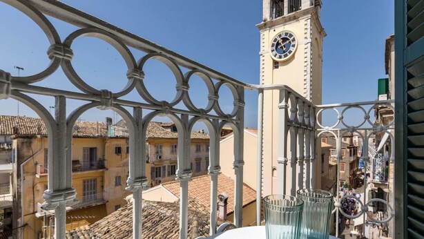A balcony with a wrought iron railing, a clock tower, and terracotta rooftops in the background. - St Spyridon Cosy Apartment By Konnect (Corfu)