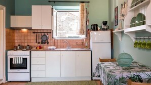 A compact kitchen with white cabinets, a stove, and a sink. There's a window with curtains, a coffee maker, and a bowl on the table. - St Spyridon Cosy Apartment By Konnect (Corfu)