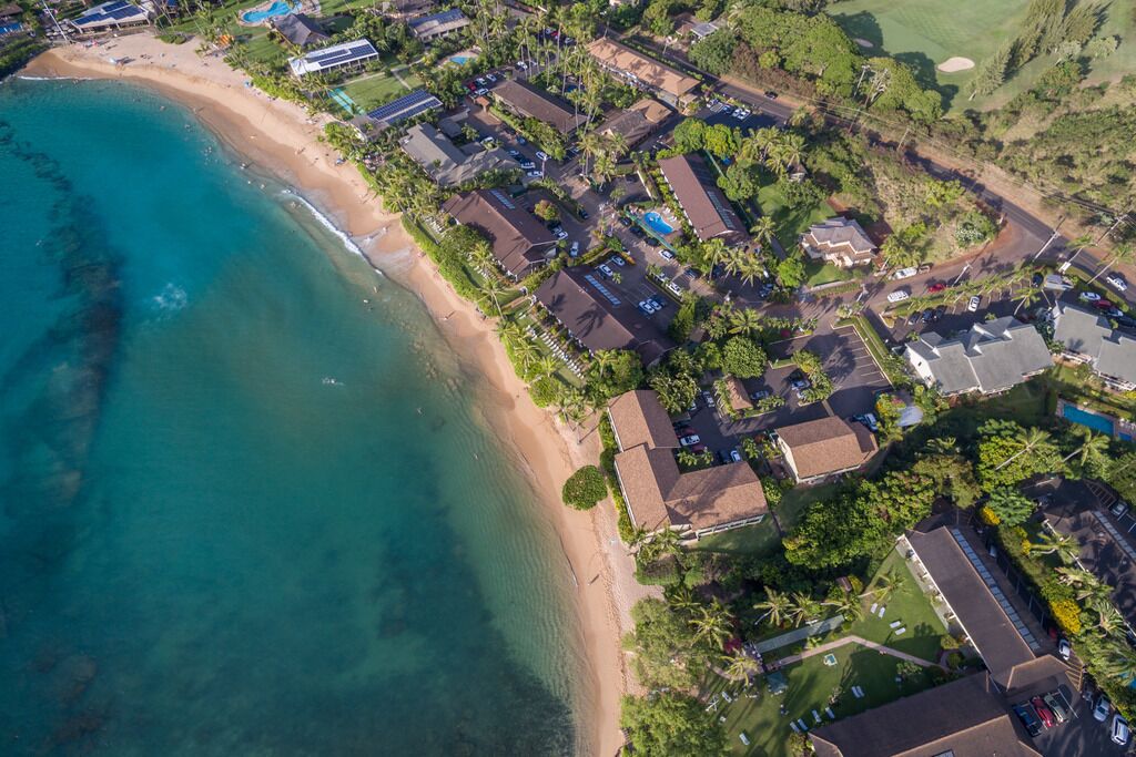 An aerial view of a coastal residential area with houses, a beach, and a golf course.