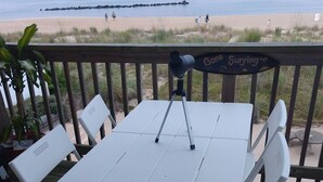 Ett vitt bord med en kamera på ett stativ, placerat på ett trädäck med utsikt över en strand.
