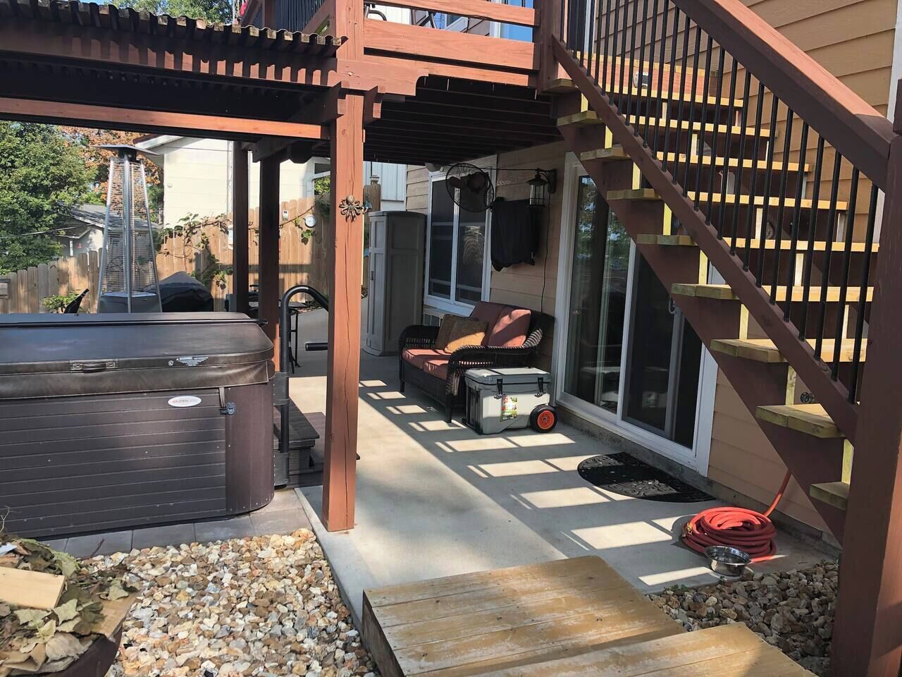 Un patio cubierto con un jacuzzi, mobiliario exterior y una escalera que lleva a un nivel superior.