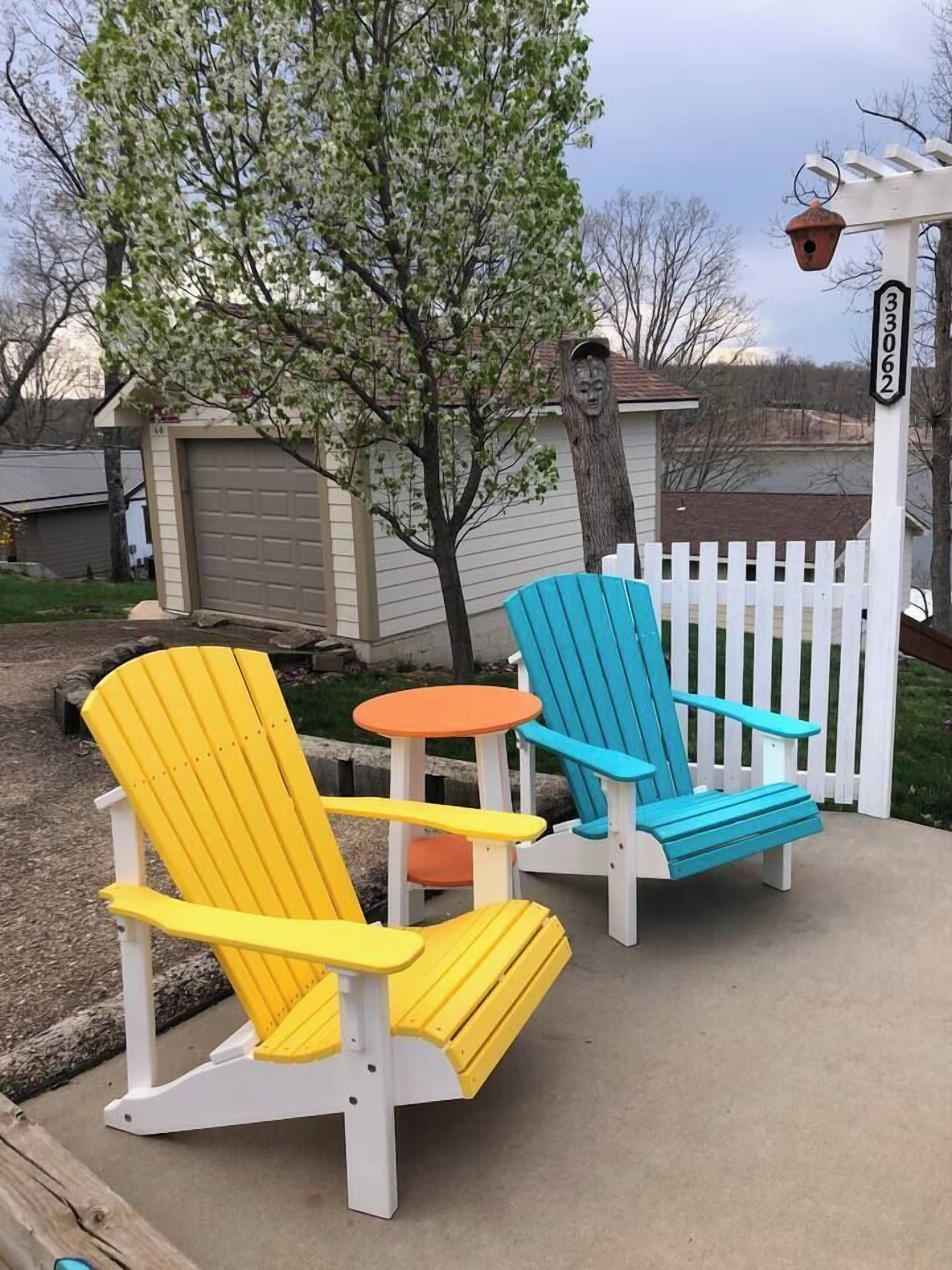 Two Adirondack chairs in yellow and blue colors, a white picket fence, and a mailbox with the number 33062.