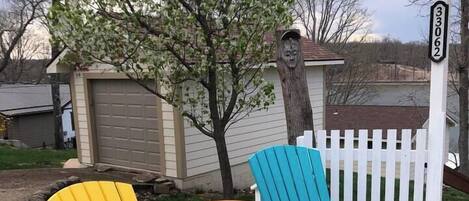 Two Adirondack chairs in yellow and blue colors, a white picket fence, and a mailbox with the number 33062.
