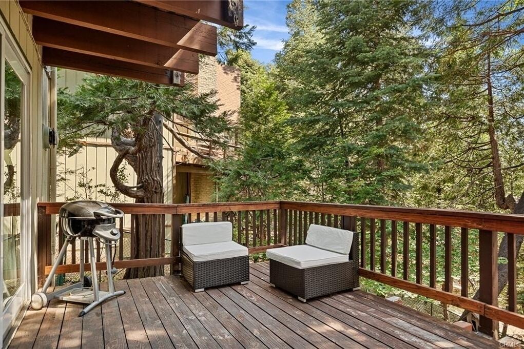 A wooden deck with two wicker chairs and a grill.