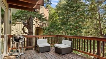 A wooden deck with two wicker chairs and a grill.