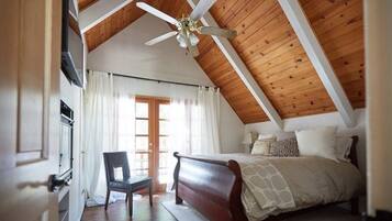 Une chambre avec un plafond en bois, un lit, une chaise et une fenêtre avec des rideaux.
