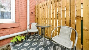 Eine Terrasse mit zwei Korbstühlen, einem kleinen Tisch, einer Ziegelwand und einem Holzzaun.