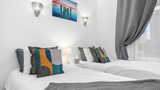 Ein Hotelzimmer mit zwei Betten, einer grauen Decke, einem Gemälde und einem Fenster mit Vorhängen.