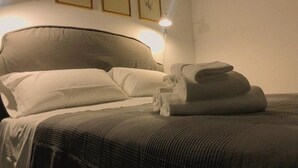 A neatly made bed with pillows and folded towels, a headboard, and framed artwork on the wall. - Torre Tresca 2 (Bari)