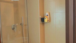 A glass-enclosed shower with a towel hanging on the door, a handheld showerhead, and a shelf with toiletries. - Torre Tresca 2 (Bari)