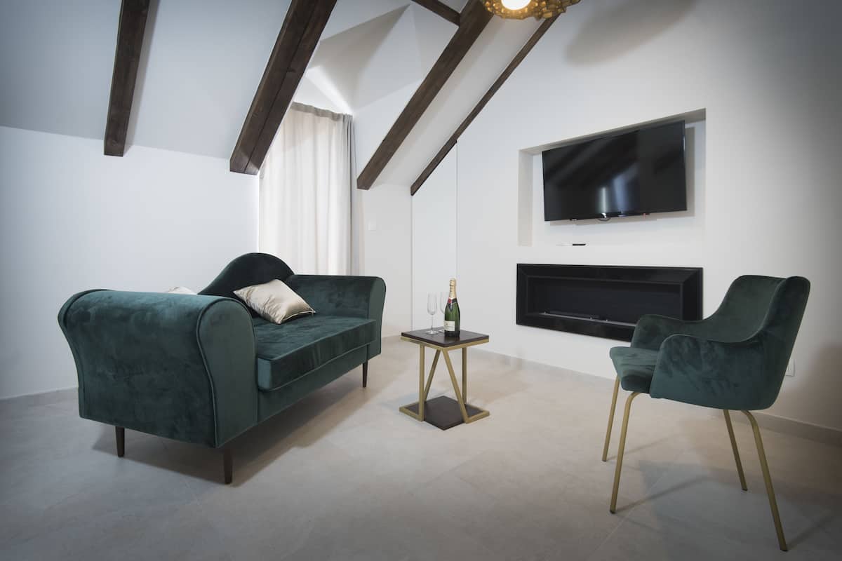 A modern living room with a green sofa, a matching armchair, a small table with a bottle, and a flat-screen TV mounted on the wall.