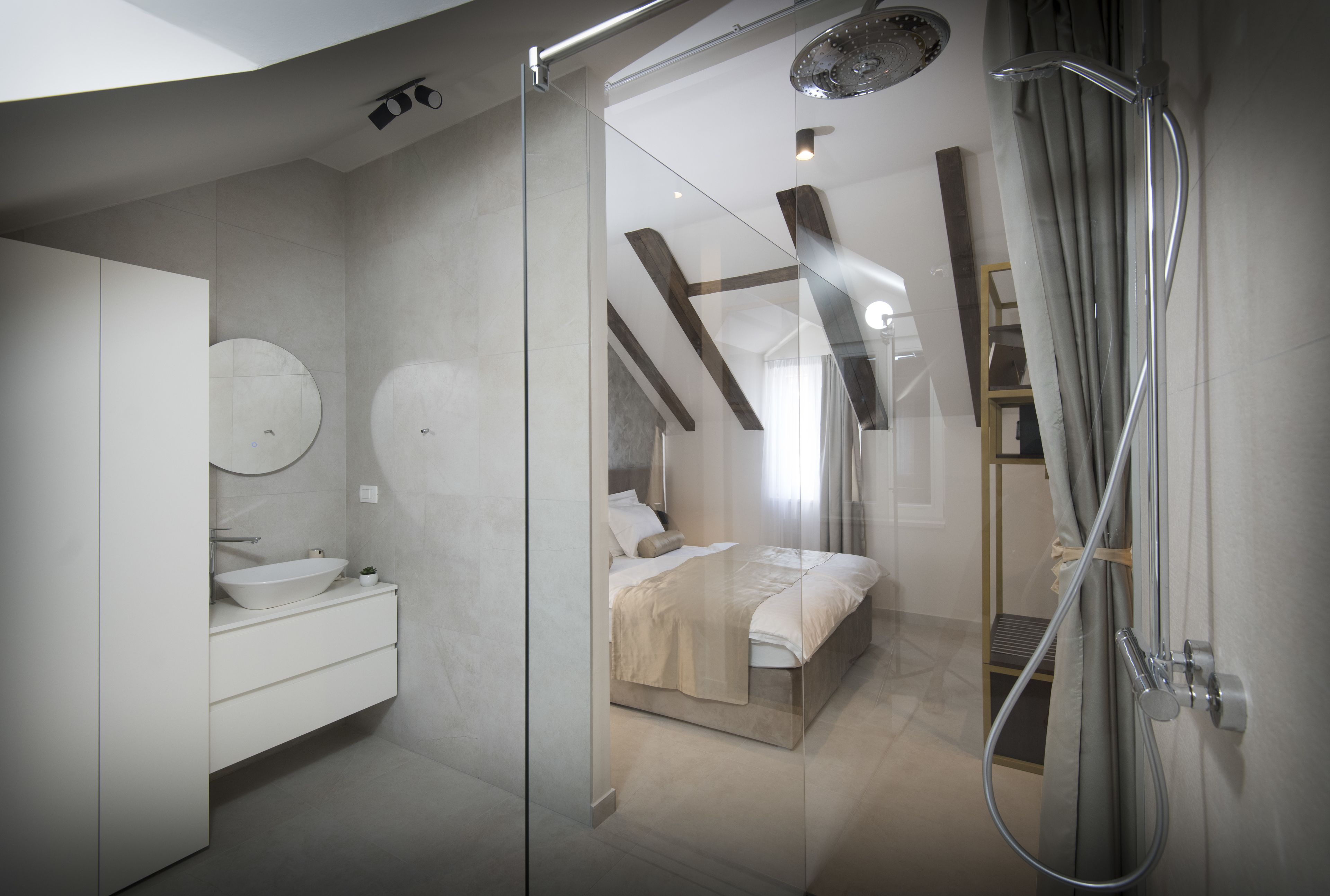 Ein modernes Badezimmer mit einer Glaskabine zur Dusche, einem weißen Waschbecken und einem Bett mit Holz Kopfteil.