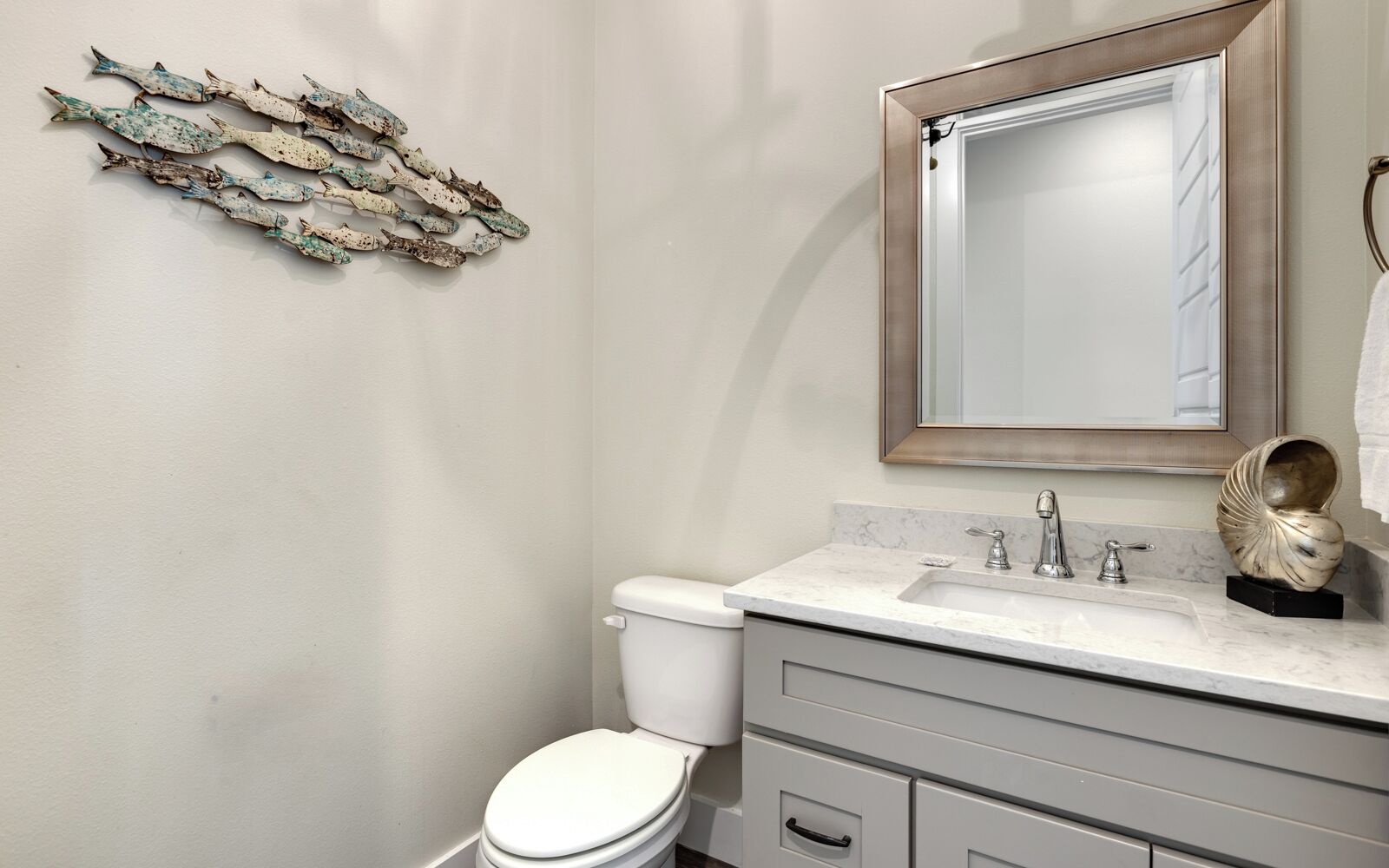 A bathroom with a toilet, sink, mirror, and decorative fish wall art.