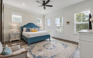 A bedroom with a blue headboard, a bed with white bedding, a nightstand with a lamp, a chair, and a large patterned rug.