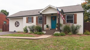 Ein eingeschossiges Haus mit Veranda, einer blauen Tür und einer amerikanischen Flagge.