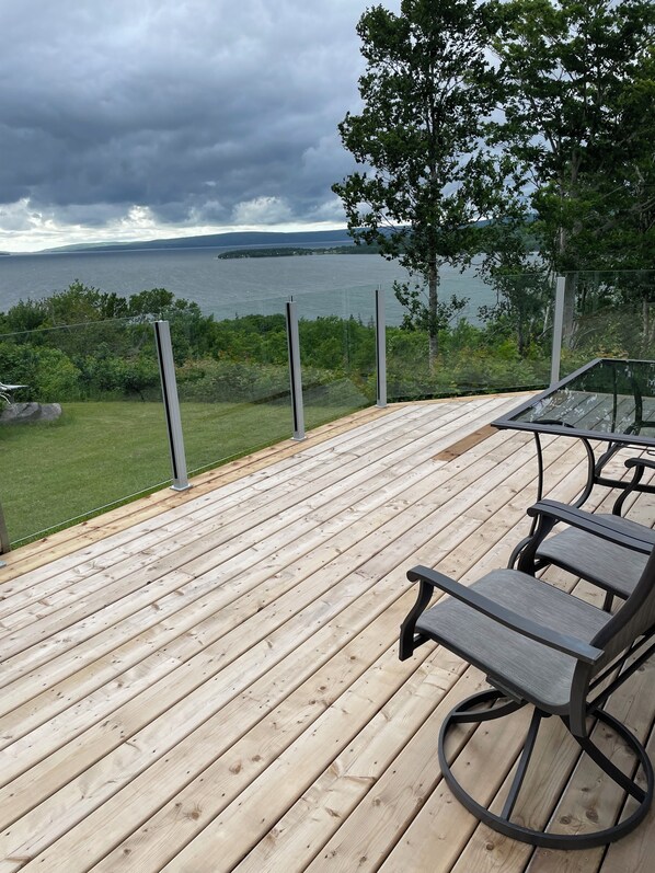Une terrasse en bois avec une table et des chaises en verre, donnant sur une étendue d’eau et une végétation luxuriante.
