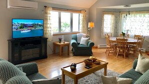 En stue med fjernsyn, sofa, sofabord, spisebord med stole og en loftsvifte.