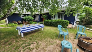 An outdoor dining area with a table set for four, surrounded by chairs, in front of a house with a dark facade and large windows. - Village home in Suttons Bay. Walk to everything. Air, grill, WIFI (Suttons Bay)