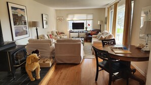 A living room with a fireplace, sofas, a TV, and a dining area with a table and chairs. - Village home in Suttons Bay. Walk to everything. Air, grill, WIFI (Suttons Bay)
