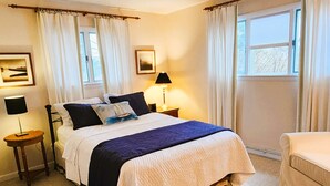 A neatly arranged bedroom with a bed, bedside lamps, a chair, and a window with curtains. - Village home in Suttons Bay. Walk to everything. Air, grill, WIFI (Suttons Bay)