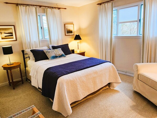 A neatly arranged bedroom with a bed, bedside lamps, a chair, and a window with curtains.