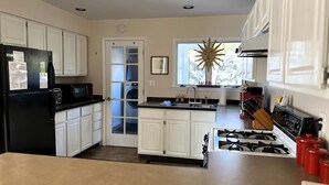 A kitchen with white cabinets, a black refrigerator, a stove, and a window with a sun decoration. - Village home in Suttons Bay. Walk to everything. Air, grill, WIFI (Suttons Bay)