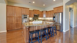 A spacious kitchen with wooden cabinets, a central island with stools, stainless steel appliances, and a tiled floor. - Group-Friendly Estrella Gem: Hike, Cheer & Explore (Goodyear)