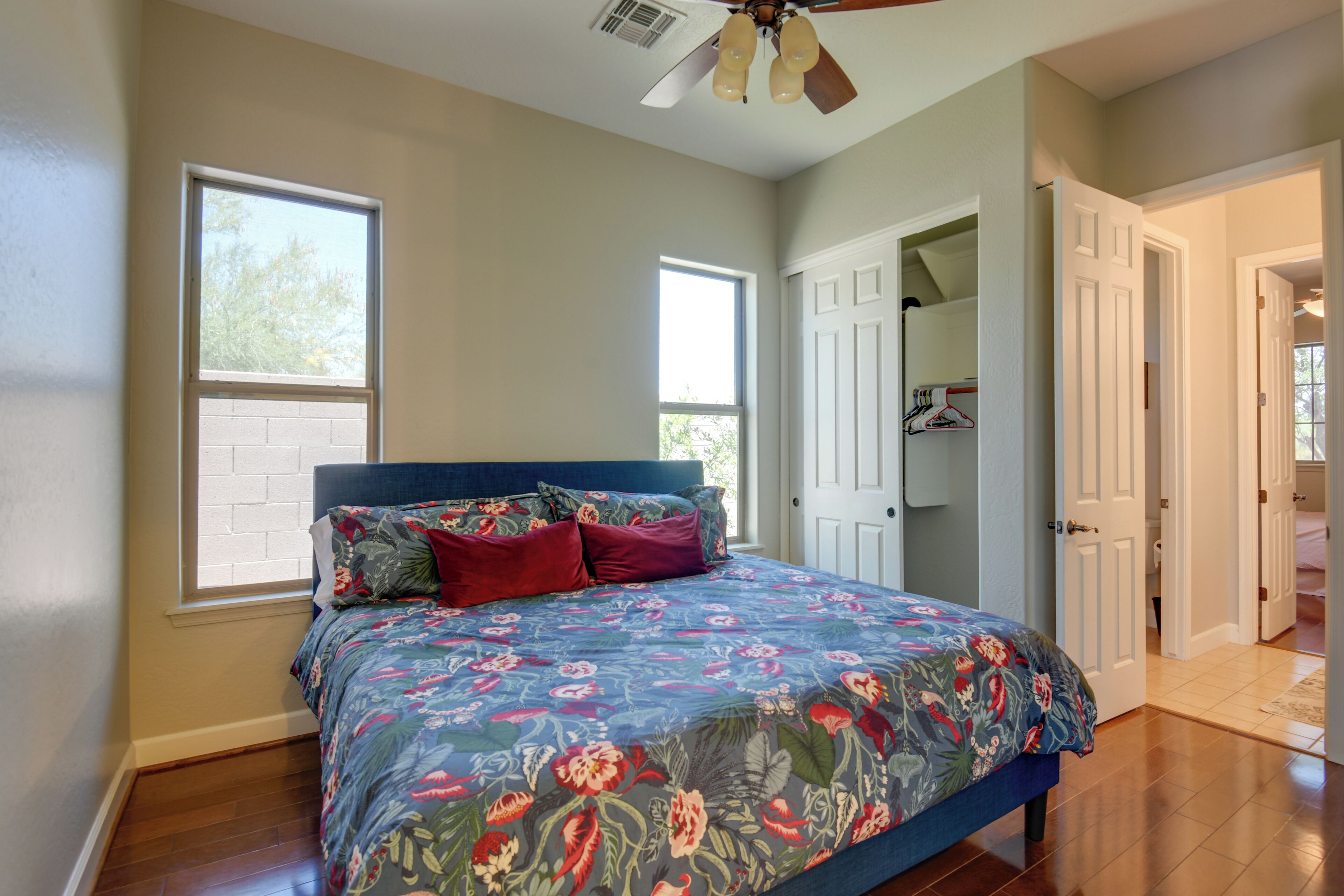 A bedroom with a floral bedspread, a ceiling fan, and a view of the outside through a window.