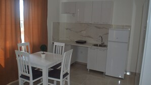 A compact kitchen with white cabinets, a small sink, and a refrigerator. There is a dining table with chairs and a potted plant. - PERAK apartments Tivat (Tivat)