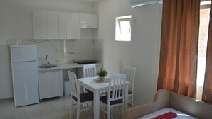 A compact kitchen with white cabinets, a built-in oven, and a small window. - PERAK apartments Tivat (Tivat)