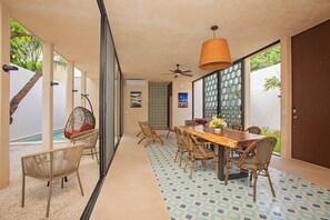 A modern dining area with a wooden table, wicker chairs, and a hanging chair by a pool.