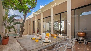 An outdoor dining area with a wooden table, chairs, a barbecue grill, and a pool in the background.