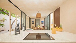 A modern kitchen with an induction cooktop, a dining area with a table and chairs, and a view of the outdoors through large windows.