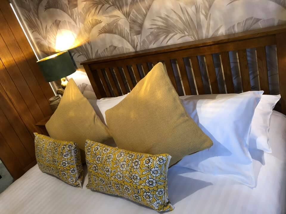 A bed with white linens and two decorative pillows, one with a yellow and white floral pattern.