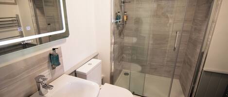 Un baño moderno con ducha de vidrio, lavamanos blanco y inodoro.