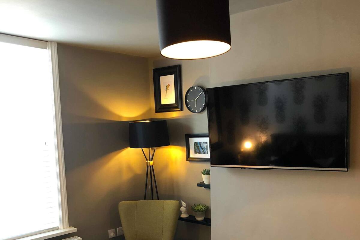 A bedroom with a bed, a chair, a TV, a lamp, and a window.