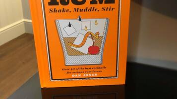 A book titled 'RUM' with a cover illustration of a cocktail shaker, a muddle, and a stirrer.