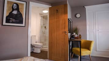 Ein Schlafzimmer mit einem Bett, einem Holzschrank, einem gelben Sessel, einem Badezimmer mit Toilette und einem gerahmten Kunstwerk an der Wand.