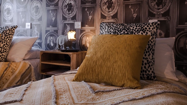 A bedroom with a patterned wallpaper, a wooden nightstand, and a bed with patterned bedding. - The Wheatsheaf Inn (Nottingham)