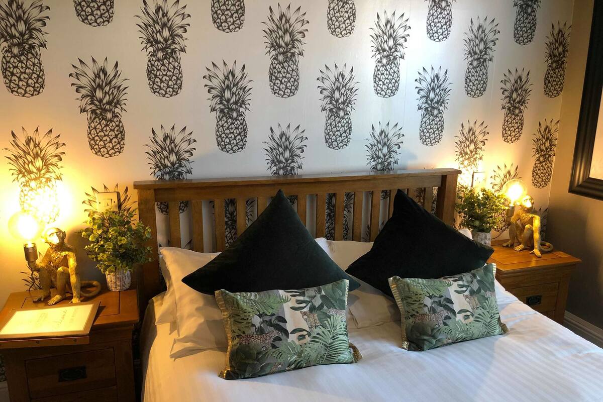 A hotel room with a bed, two nightstands, a wooden headboard, and a pineapple-themed wallpaper.