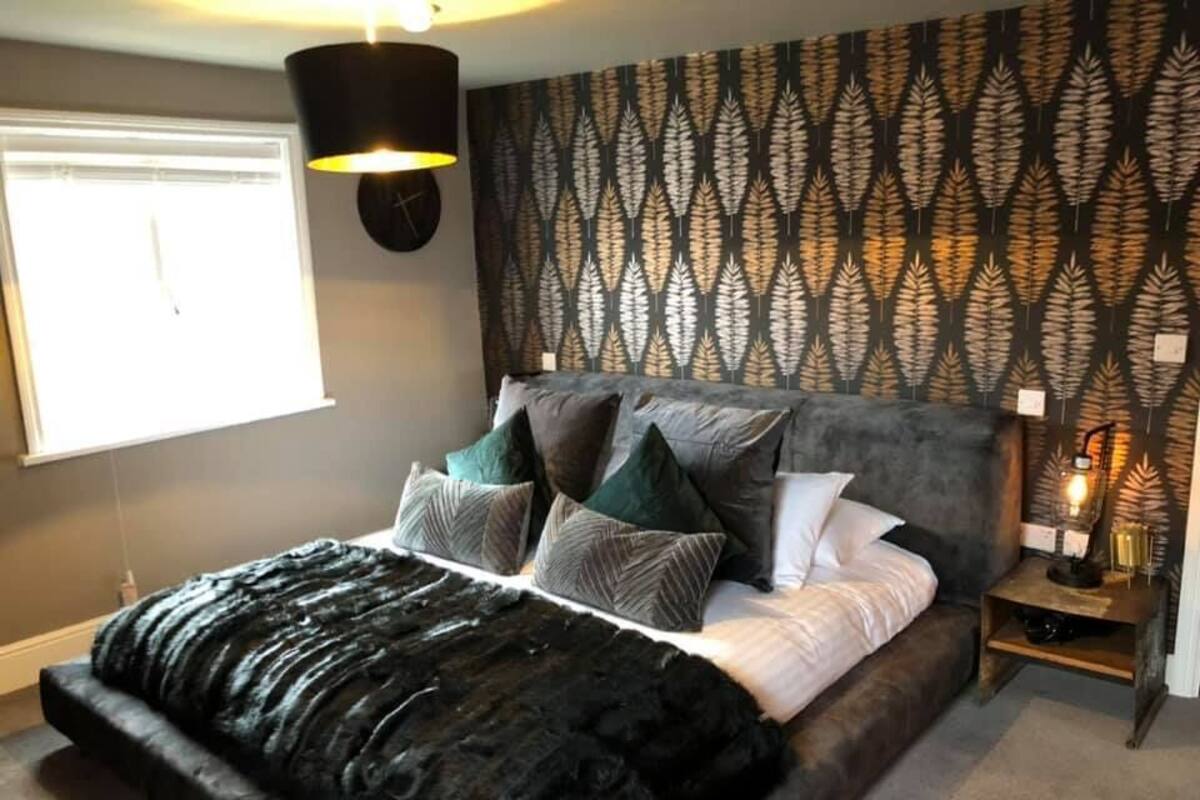 A bedroom with a bed, pillows, a nightstand, a wall clock, and a patterned wallpaper.