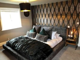 A bedroom with a bed, pillows, a nightstand, a wall clock, and a patterned wallpaper.