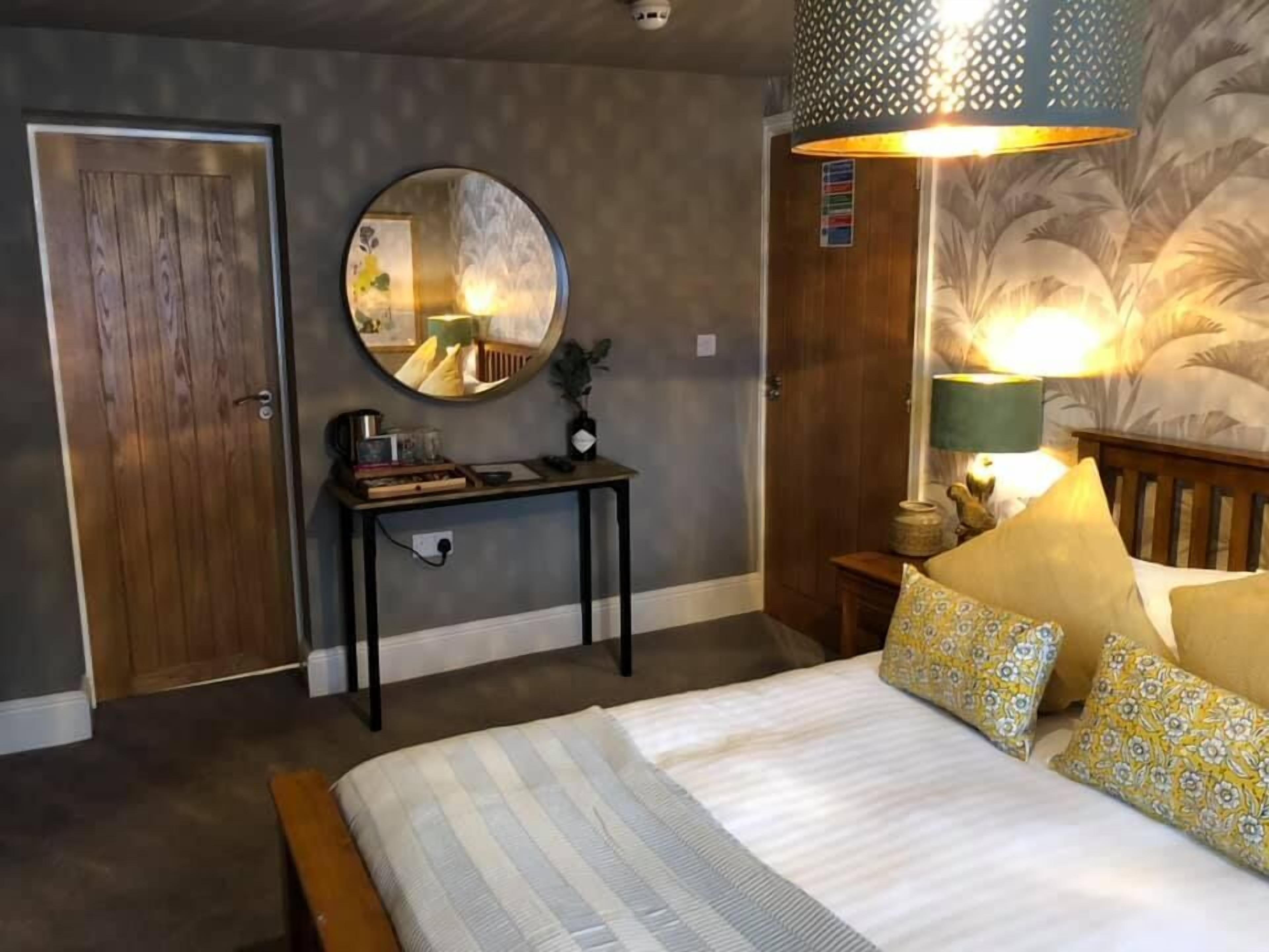 Un dormitorio con una cama, un espejo redondo, una mesita de noche, un escritorio y una puerta.