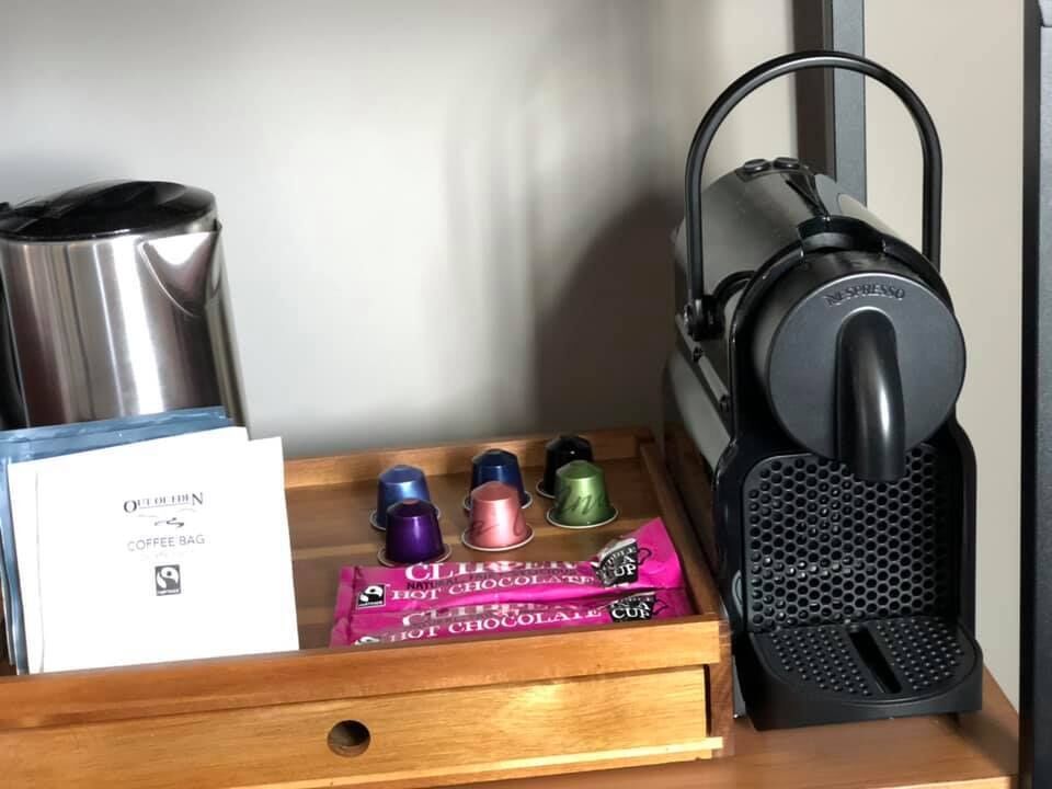 Een koffiezetapparaat, een roestvrijstalen pan, en een lade met koffiezakjes en kleurrijke mokken.