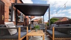 An outdoor patio with wicker furniture, a wooden table, and a black canopy. - The Wheatsheaf Inn (Nottingham)