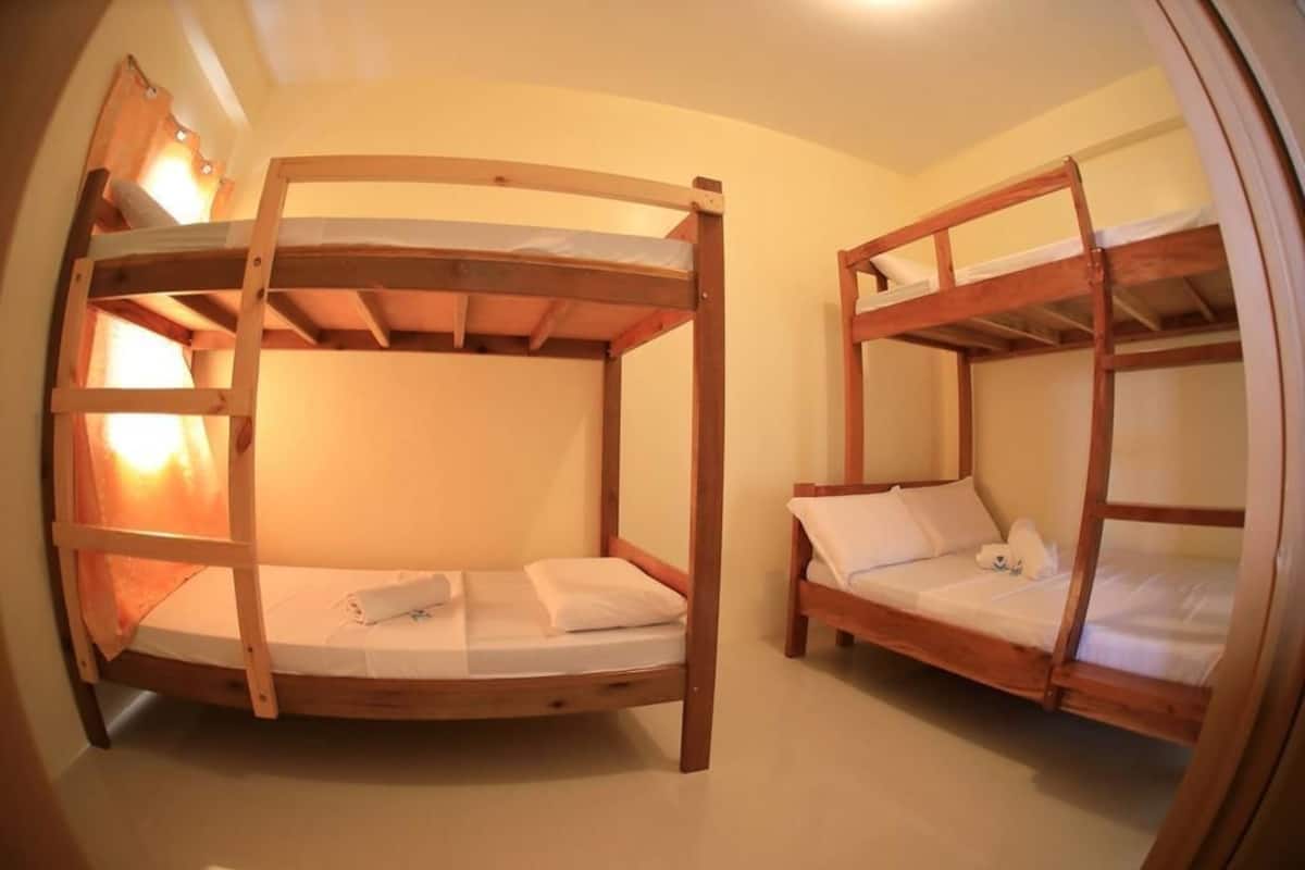 A dormitory room with two bunk beds, each with a wooden frame and white bedding.