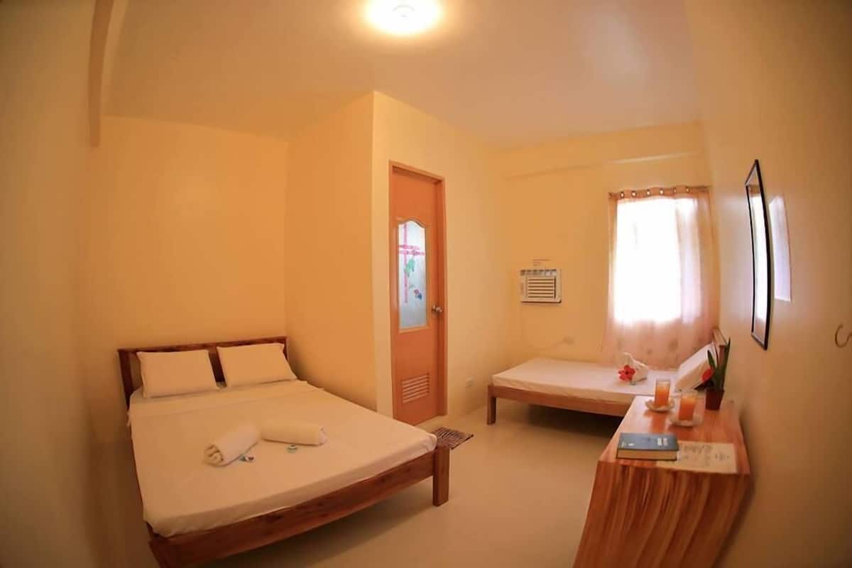 A bedroom with two single beds, a wooden nightstand with a book and a glass, and a window with curtains.
