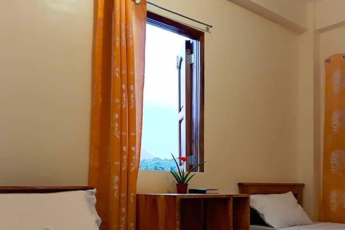 A hotel room with two beds, a wooden desk, and a window with curtains.