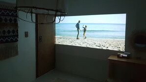 A room with a large window overlooking a beach, a bed, a small table, and a wall with a patterned tapestry. - Hotel Elephant (Busan)