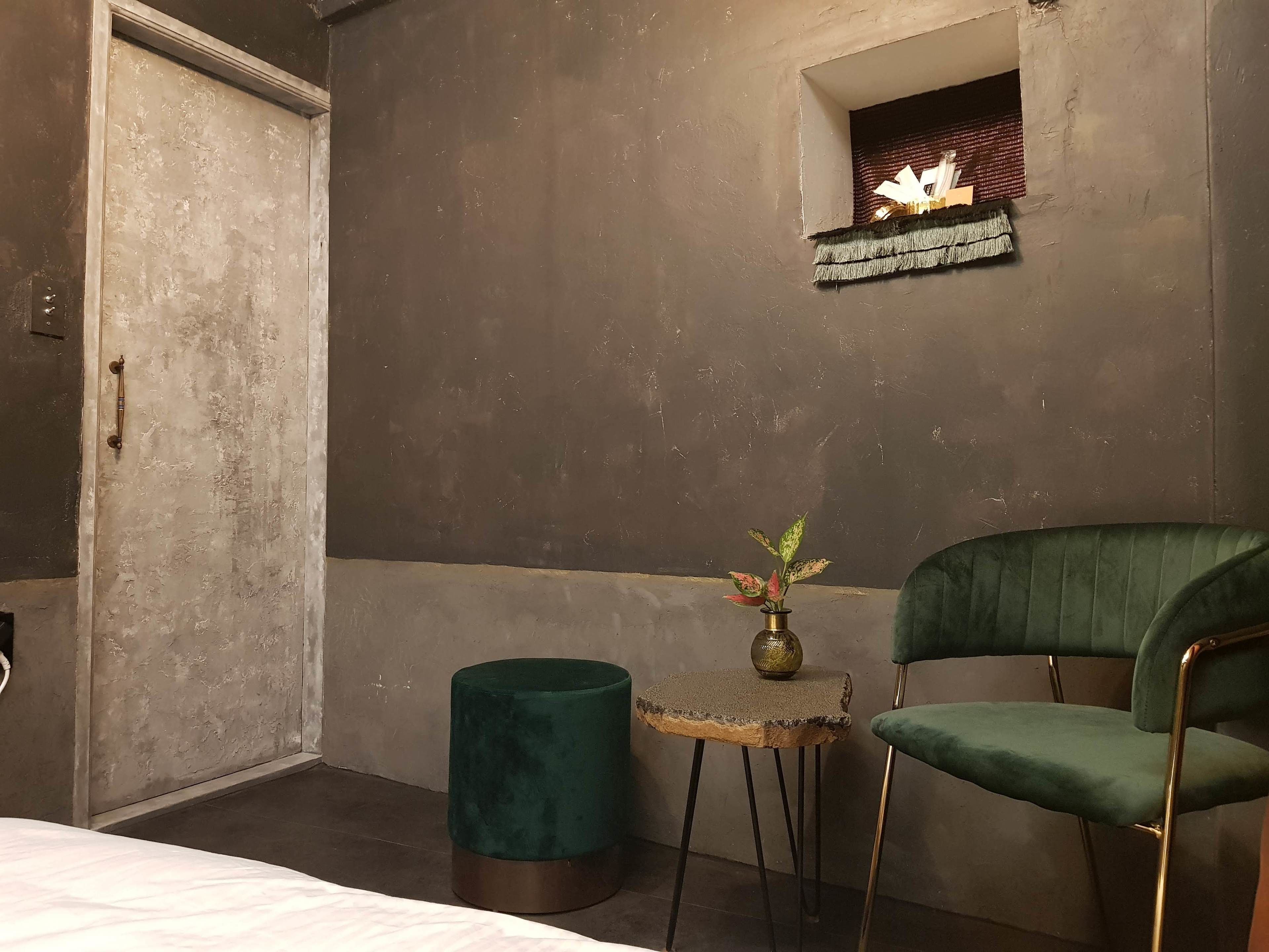 A room with a green chair, a small table with a plant, and a textured wall.